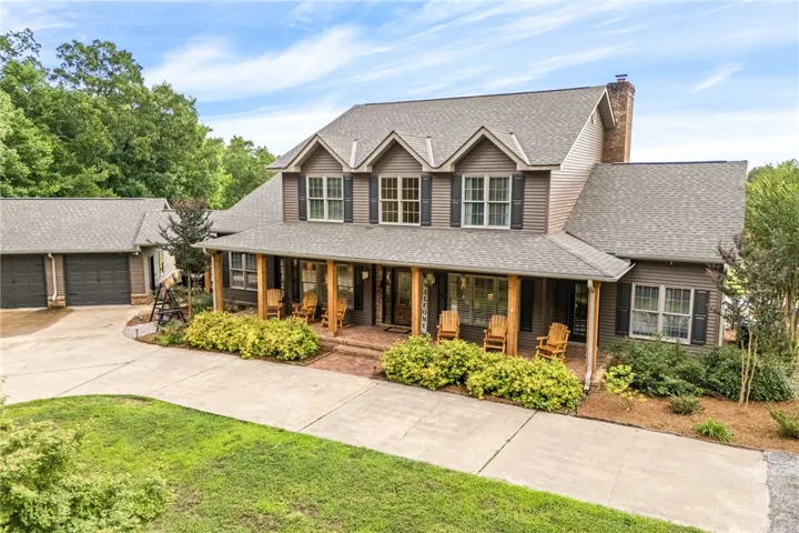 A spacious home welcomes with a wide covered front porch, featuring gabled dormers and an attached garage.