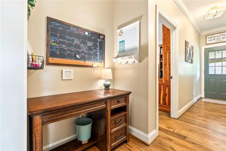 Rich hardwood flooring guides you through this functional hallway, featuring a convenient desk and organized wall storage.