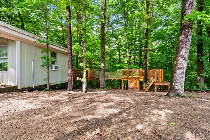 A secluded forest setting features a charming treehouse play structure connected by a rope bridge, promising endless outdoor adventure.
