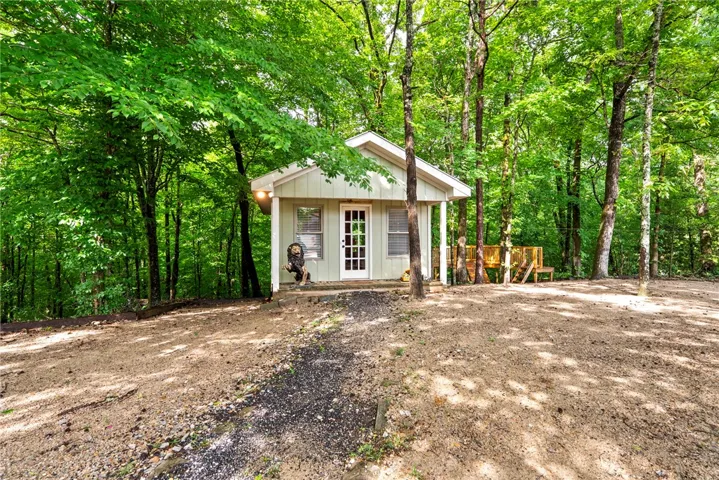 A charming cottage is nestled within a verdant forest, featuring a front entry and a wooden deck.