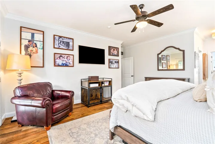 Hardwood flooring extends throughout this naturally illuminated bedroom with a ceiling fan.