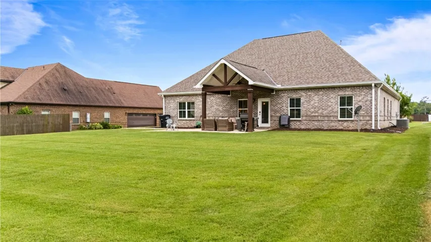 A spacious backyard with a meticulously maintained lawn, featuring a covered patio and a brick exterior home.