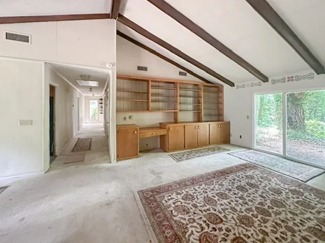 A versatile open space with high vaulted ceilings and built-in shelving, connecting to a hallway and overlooking lush greenery.