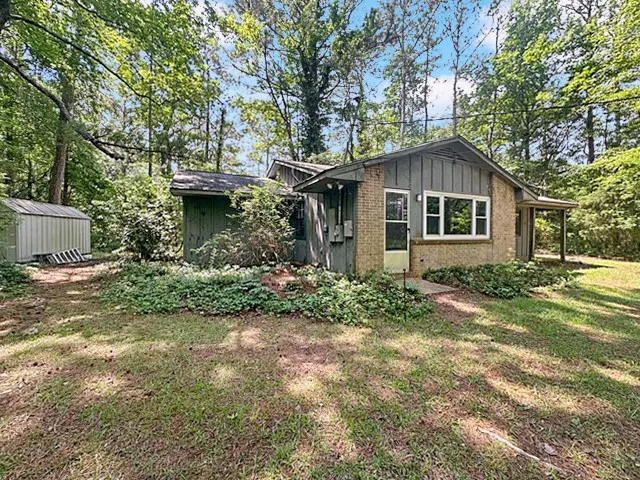 A charming brick and wood siding residence nestled amidst a verdant, mature treeline.