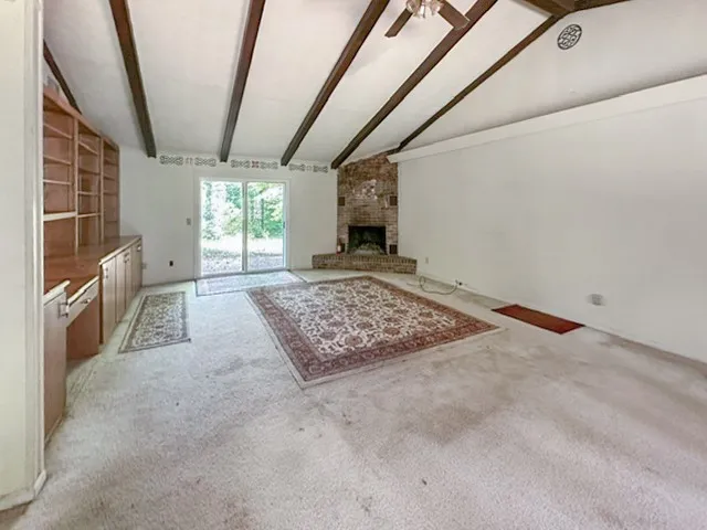 Exposed wood beams adorn the vaulted ceiling, complementing the brick fireplace and built-in shelving.