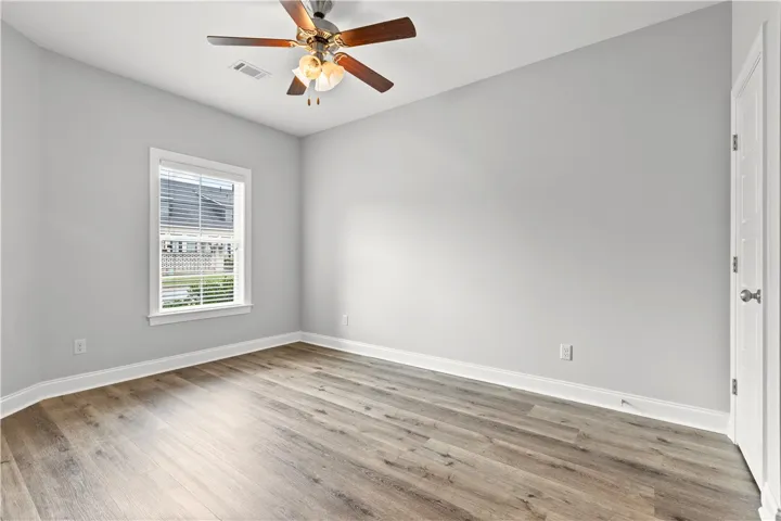 A well-lit bedroom features durable hardwood flooring and a ceiling fan for comfort.