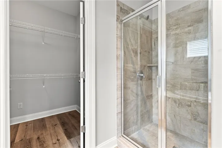 A sleek, tiled shower with a glass enclosure stands beside a functional closet, showcasing convenient living.