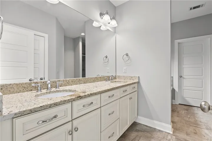 Dual vanity with granite counters and expansive mirror elevates this primary bath's functionality and elegance.