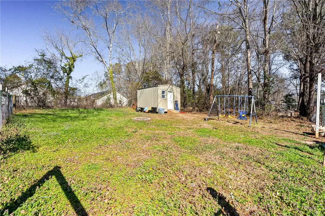 A spacious, grassy lot awaits, bordered by a fence and mature trees, featuring a storage shed and play equipment.