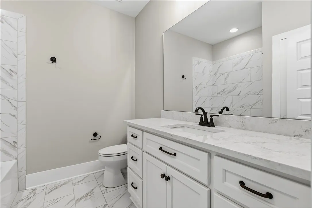 White cabinetry, elegant tile, and a large mirror illuminate this tasteful bath space.