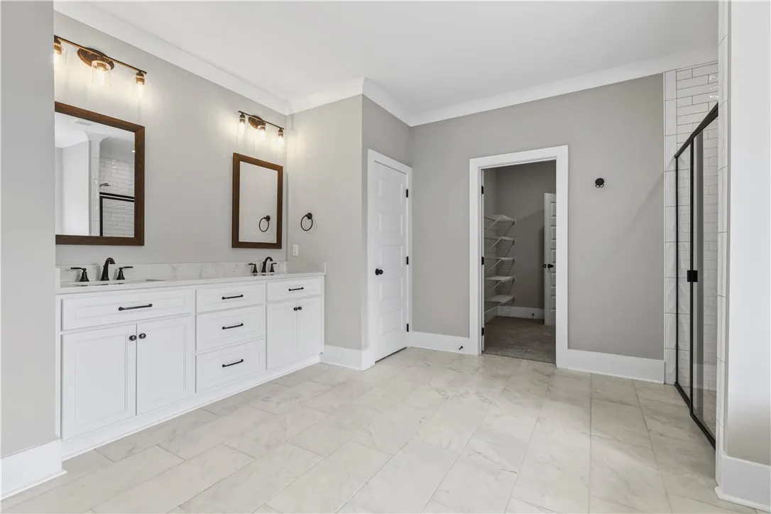 A well-appointed primary bathroom showcases dual vanities, elegant tile flooring, and convenient access to a walk-in closet and a separate shower and bathtub.