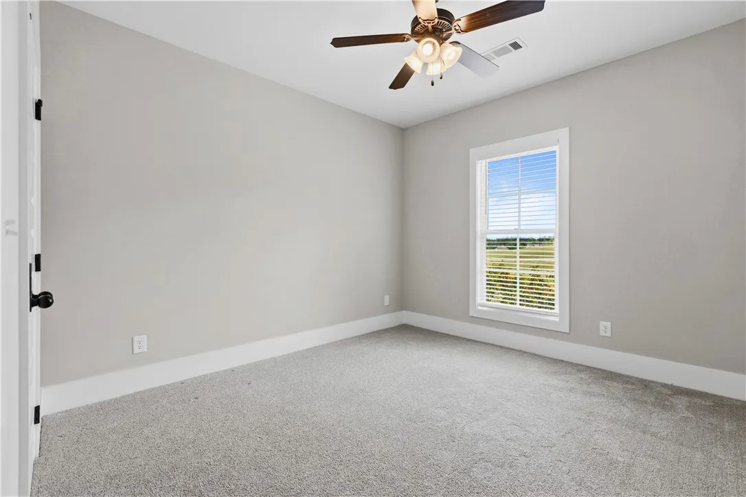 A well-lit bedroom with soft carpeting and a window offering views of the natural landscape.