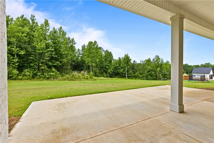 A spacious covered patio overlooks a generous backyard bordered by lush trees.