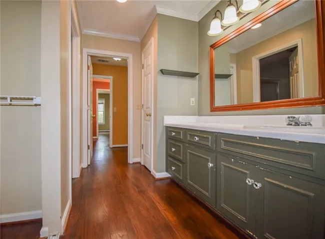 A well-lit hallway with rich wood flooring leads to a functional bathroom vanity.