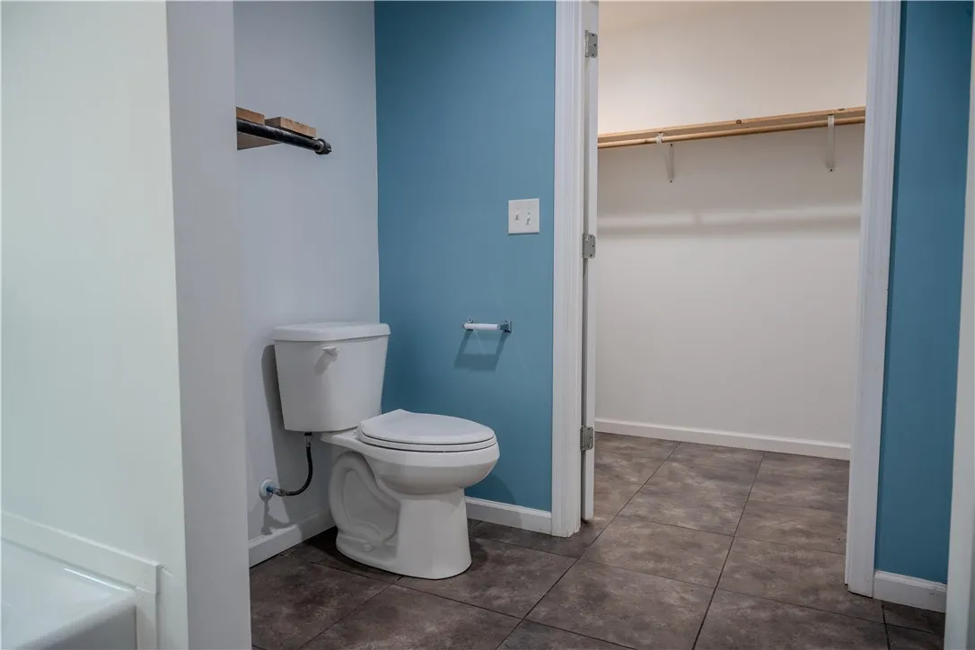 Functional bathroom featuring a commode and tiled flooring, with an adjacent closet for storage.