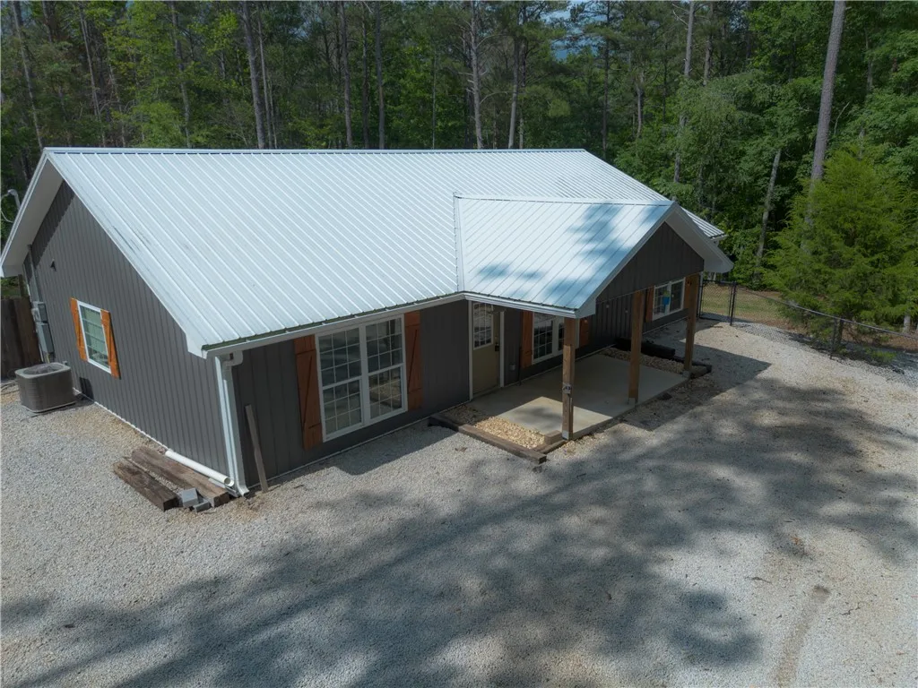 A charming cottage amidst tall trees, boasting a modern metal roof and rustic wooden shutters.