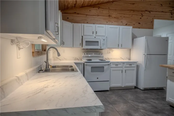 A pristine kitchen offers ample counter space and modern appliances set against a rustic wood-paneled ceiling.