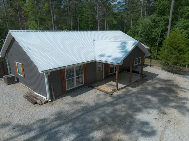 A charming cottage amidst tall trees, boasting a modern metal roof and rustic wooden shutters.
