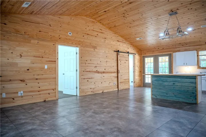 A spacious room features vaulted wood ceilings, a kitchen island, and French doors leading to the exterior.