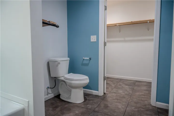 Functional bathroom featuring a commode and tiled flooring, with an adjacent closet for storage.