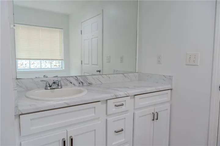 White cabinetry provides ample storage beneath a sleek, marbled vanity in this updated primary bathroom.