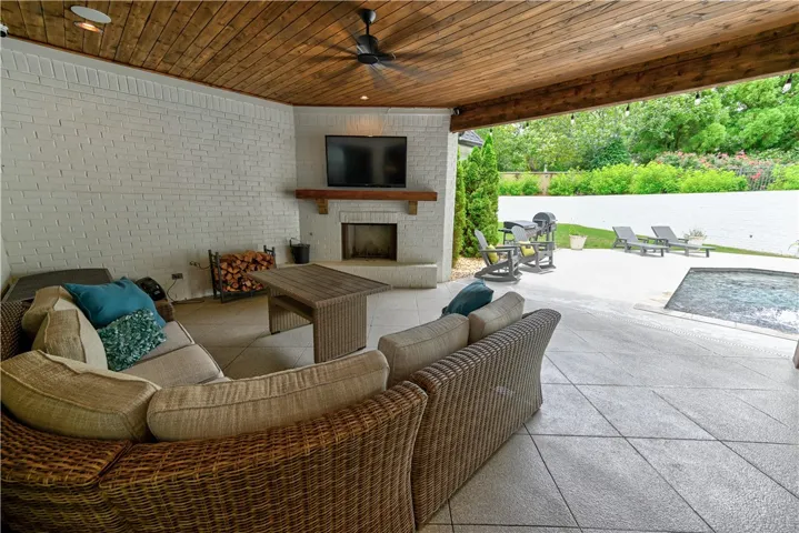 An inviting all-season outdoor living area features a cozy wood-burning fireplace and beautiful wood-plank ceiling with integrated speakers.