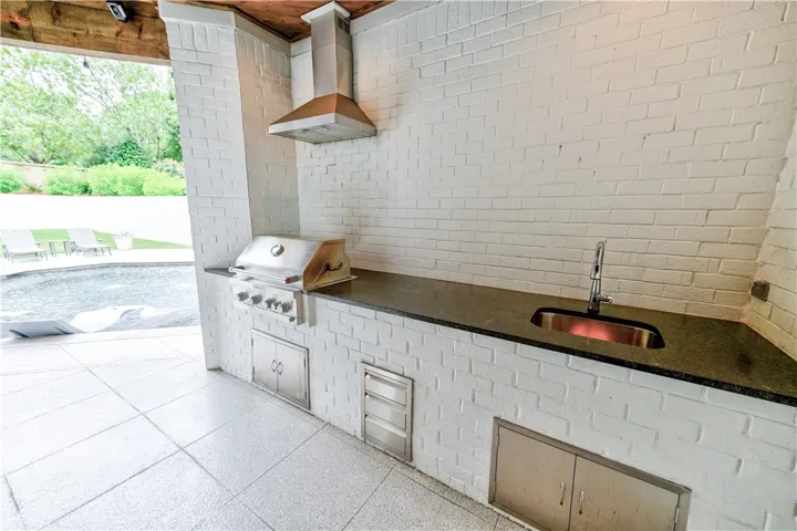 Outdoor kitchen with built-in gas grill, hood, sink, storage, plus plenty of prep space.