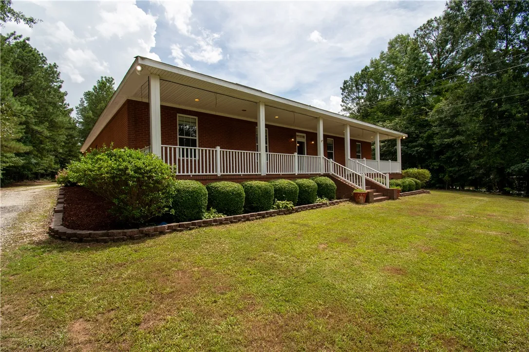 A classic brick residence, shaded by mature trees, features a long, inviting covered front porch.