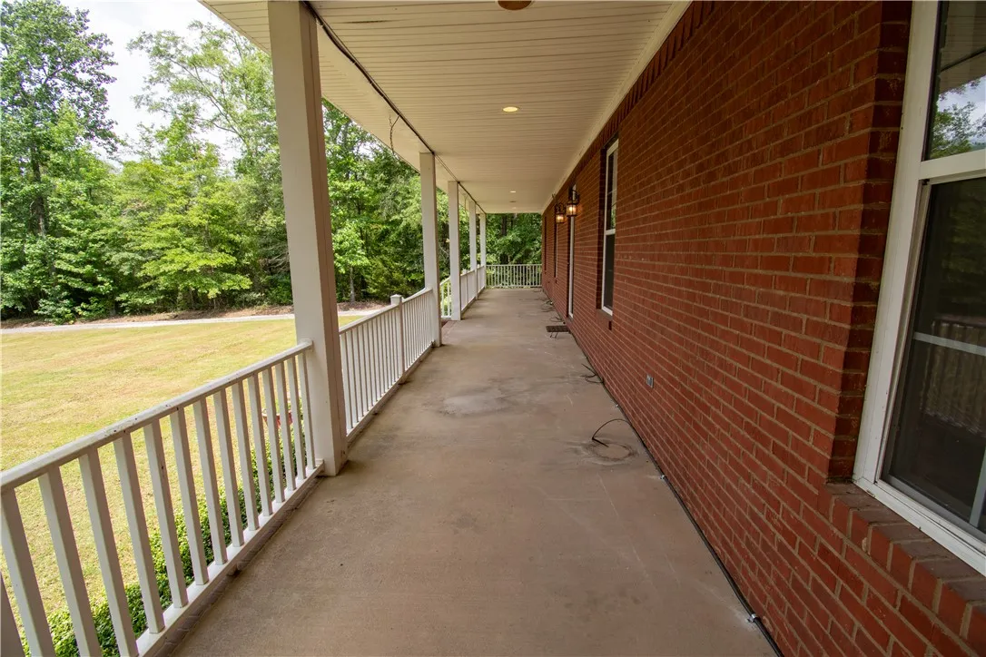A deep covered porch stretches along a brick exterior, offering peaceful views of the surrounding natural landscape.