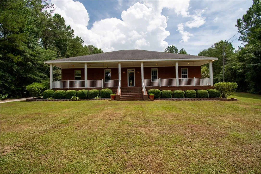 A classic brick facade is framed by a generous porch, inviting relaxation amidst mature trees.