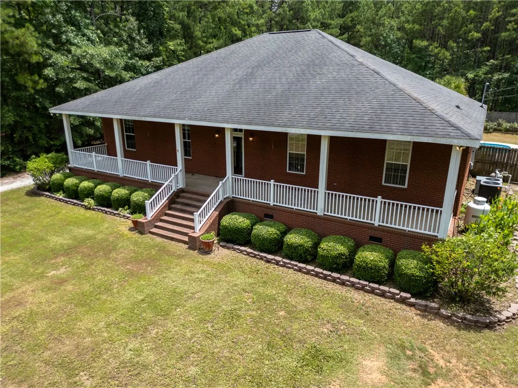 A well-maintained brick exterior home features a welcoming covered porch and lush, manicured landscaping.