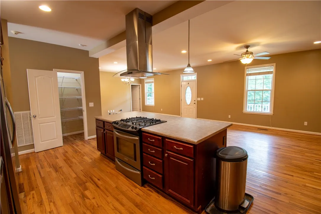 An open-concept kitchen and living area feature a central island with a gas range and gleaming hardwood floors.