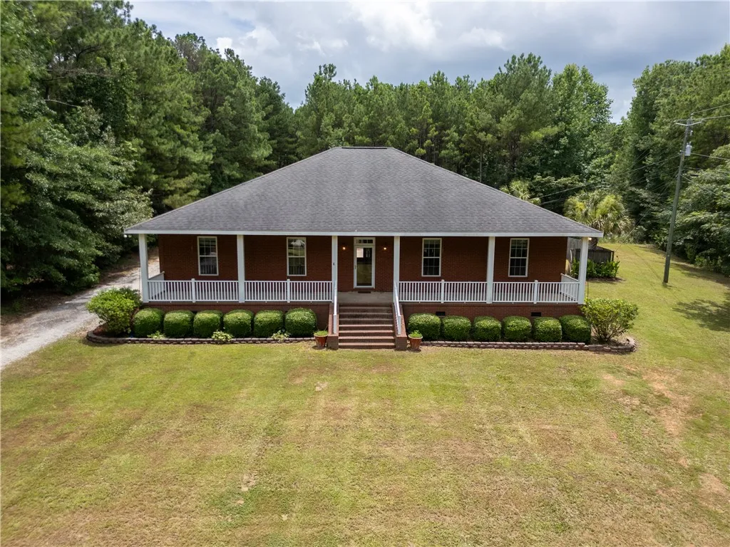 A classic brick ranch home sits serenely amidst a lush, wooded landscape with a welcoming covered front porch.