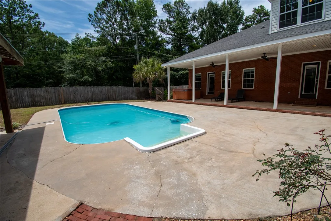 An inviting backyard oasis features a clear blue in-ground pool, expansive concrete patio, and brick-sided home with covered porch.