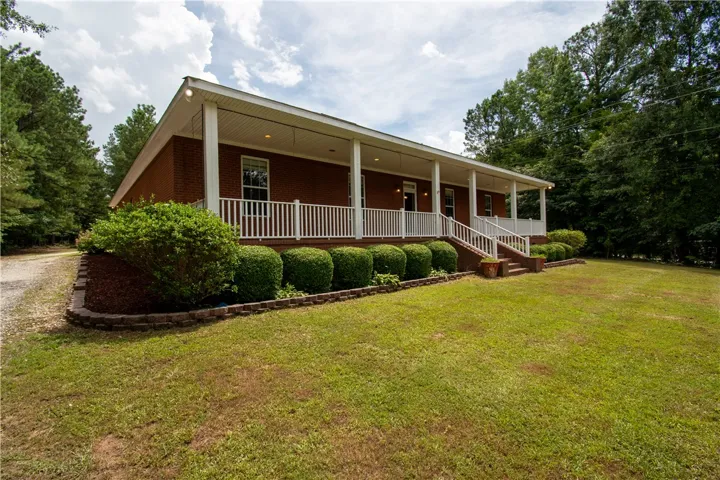 A classic brick residence, shaded by mature trees, features a long, inviting covered front porch.