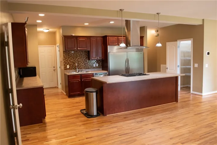 An open concept kitchen features warm wooden cabinetry, stainless steel appliances, and a central island with a built-in cooktop.