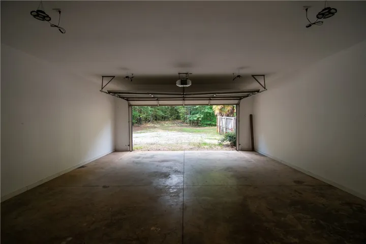 A spacious, clean garage with an open door leads to a verdant outdoor area.