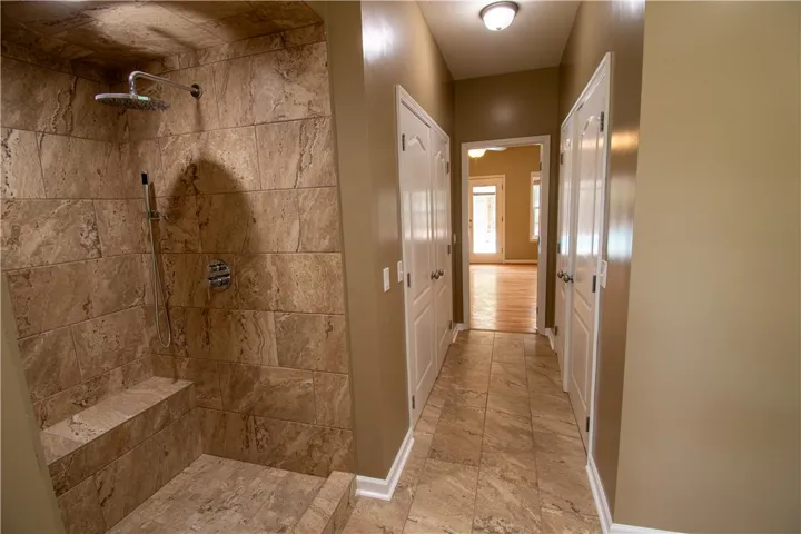 A spacious, naturally illuminated hallway featuring rich tile flooring and easy access to a luxurious, tiled walk-in shower.