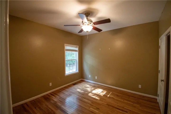 Well-lit room featuring rich hardwood flooring and a functional ceiling fan for optimal air circulation.