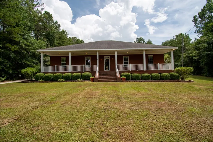 A classic brick facade is framed by a generous porch, inviting relaxation amidst mature trees.