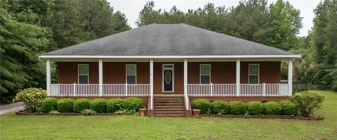 Brick facade and covered front porch create a welcoming curb appeal amidst lush greenery.