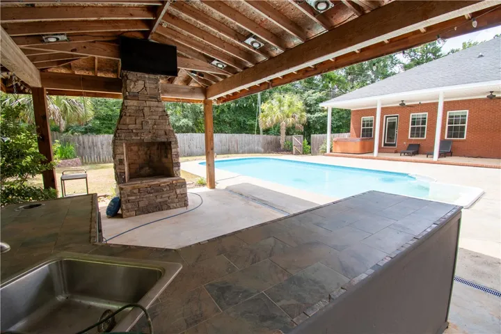 An inviting covered patio offers a stone fireplace and built-in sink next to a sparkling in-ground pool.