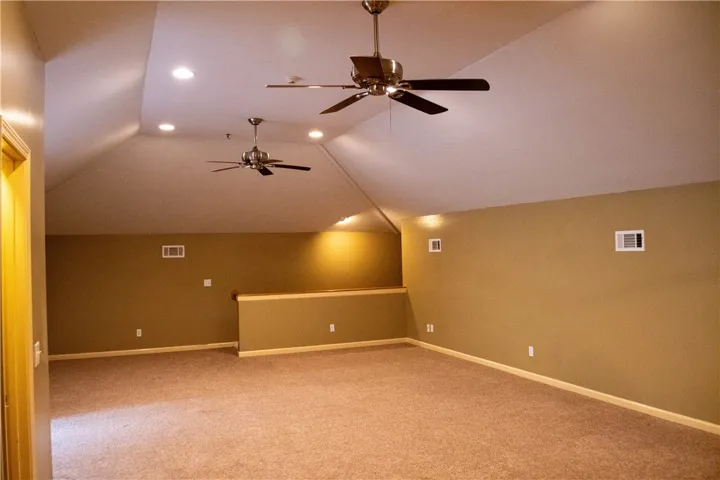 An inviting room boasts vaulted ceilings with recessed lighting and soft carpeting, creating a comfortable living space.