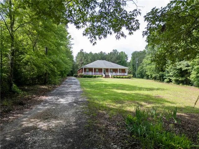A long, winding gravel driveway leads to a classic ranch-style residence surrounded by mature trees.