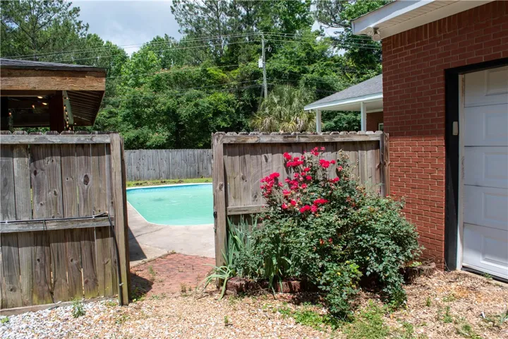 A private backyard oasis features an inviting pool, brick siding, and vibrant red rose bushes.