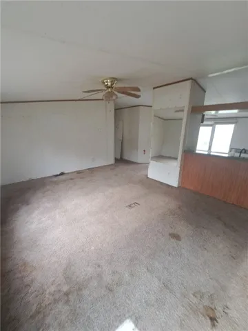 A living space offers potential with existing carpet and a ceiling fan, awaiting a fresh vision.