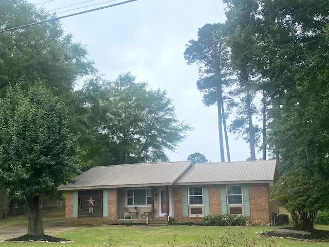 A charming single-story brick home, shaded by mature trees, invites with a welcoming front porch.
