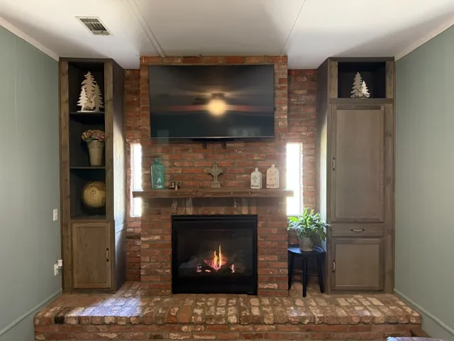A cozy living space boasts a robust brick fireplace, flanked by custom-built shelving units for organized display.