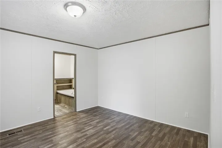 A view of the bedroom with wood plank flooring and an entryway to an adjacent bathroom featuring a built-in tub.