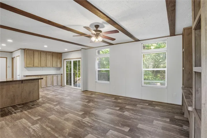 A spacious room features exposed wooden beams, durable laminate flooring, and sliding glass doors to the outside.
